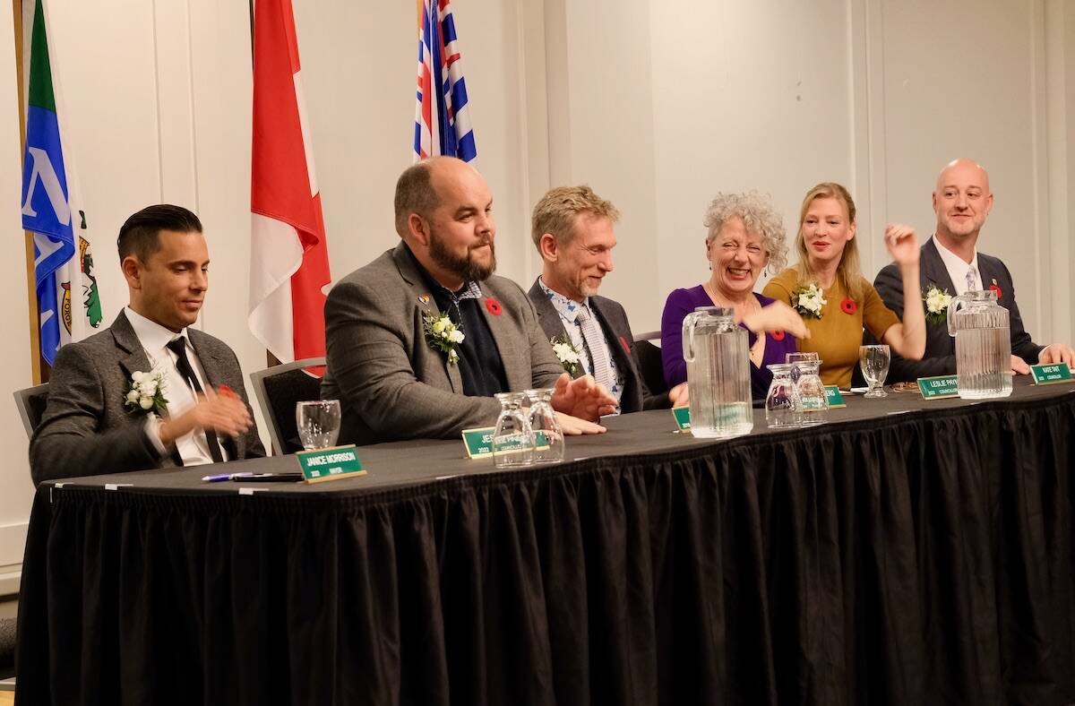 Six elected officials seated at a long panel table wearing poppies, with Canadian and British Columbia flags behind them